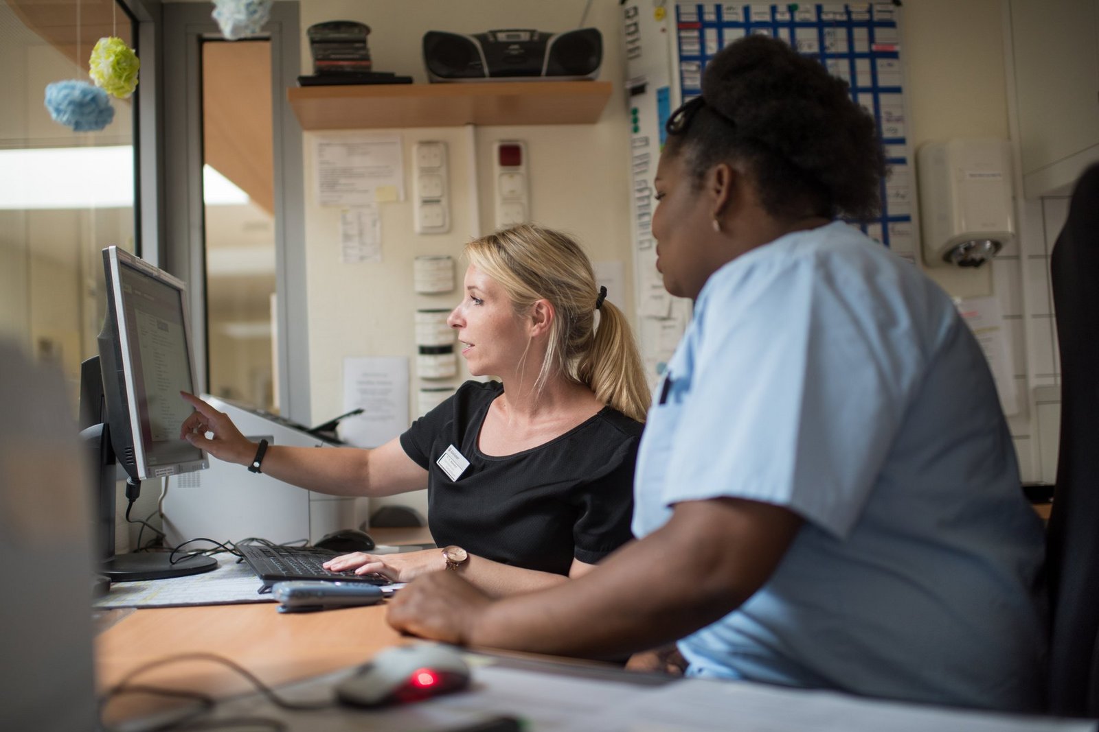 Zwei Gesundheits- und Krankenpflegerinnen arbeiten an einem Computer im Stationszimmer