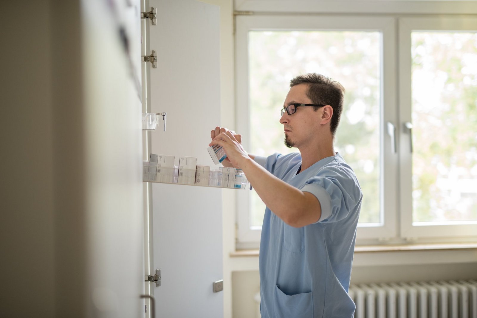 Gesundheits- und Krankenpfleger am Medikamentenschrank im Stationszimmer