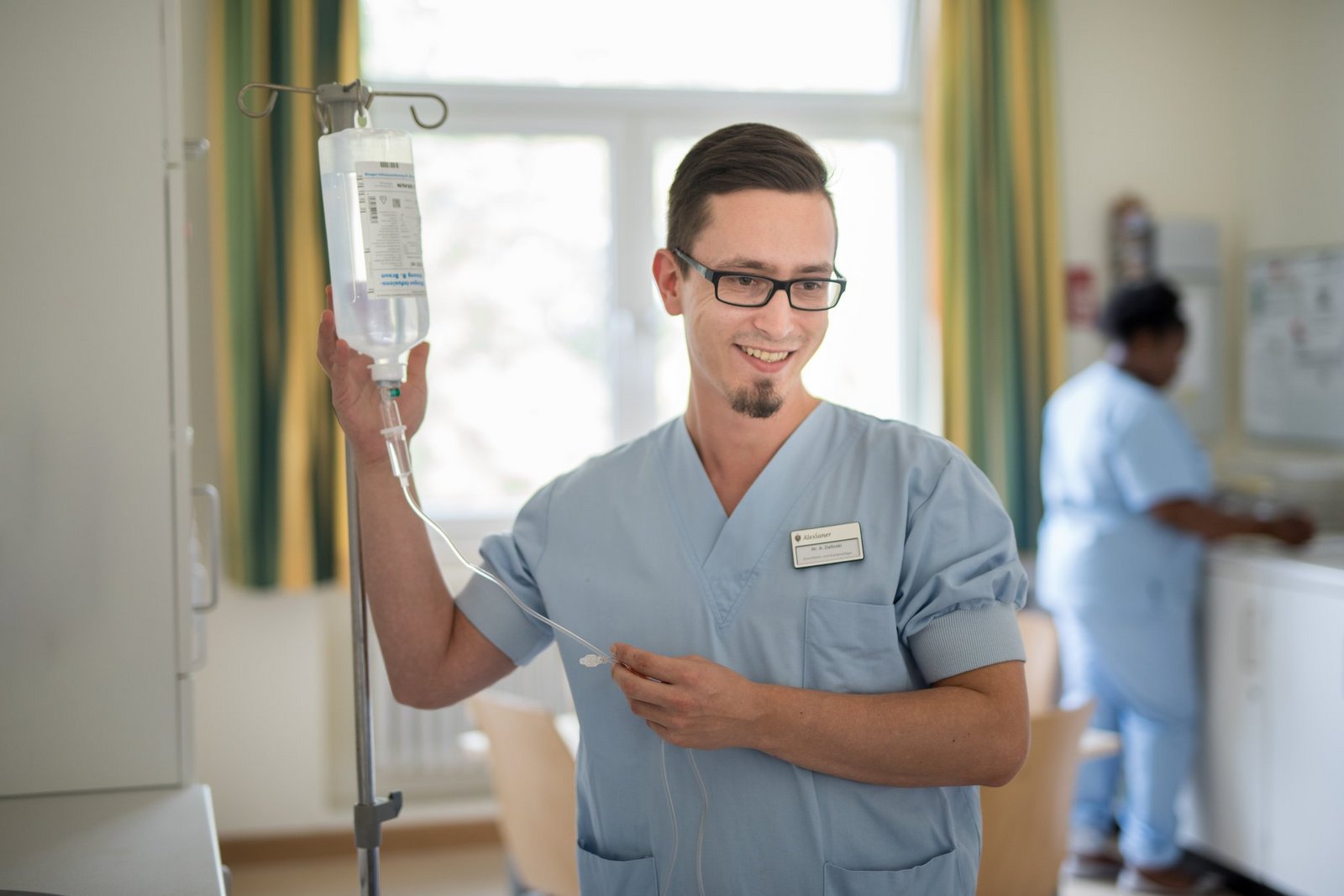 Ein Gesundheits- und Krankenpfleger mit einer Infusion, den freundlichen Blick auf einen Gesprächspartner gerichtet